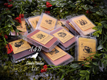 Load image into Gallery viewer, A photo showing various clamshell plastic cases with wax melt tarts inside. The cases have labels that feature a primitive sketch of each flavor or scent.