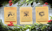 Load image into Gallery viewer, A photo showing various clamshell plastic cases with wax melt tarts inside. The cases have labels that feature a primitive sketch of each flavor or scent.